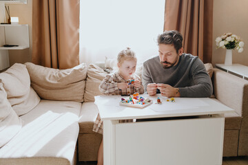 A 3-year-old girl and her father play with modeling clay in a sunny living room. Unfiltered,...