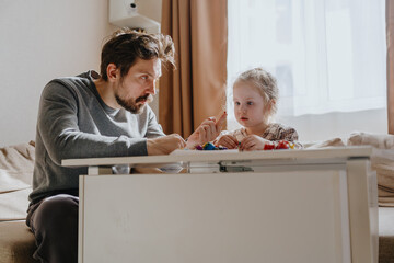A 3-year-old girl and her father play with modeling clay in a sunny living room. Unfiltered,...