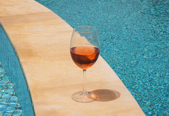Glass of chilled rosé wine on poolside edge, summer refreshment under bright sunlight,