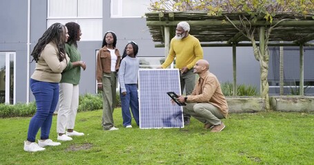 Male technicians tapping tablet and guiding diverse family sharing solar panel cable in front yard - Powered by Adobe
