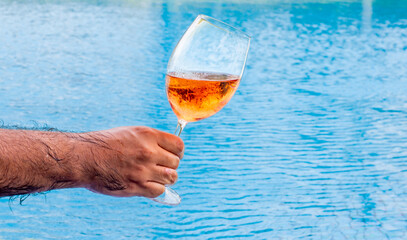 Hand holding glass of rosé wine near swimming pool edge, relaxed summer leisure moment,