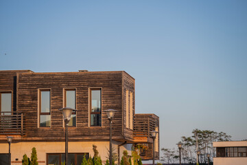 Modern wooden building with tall vertical windows stands under a clear blue sky, framed by trees and street lamps.