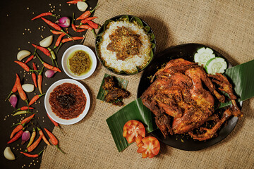 Spicy Taliwang Chicken served with warm white rice, chili sauce, fried onions, tomatoes, and cucumbers. Traditional Lombok dish, food