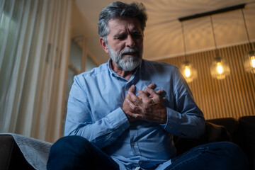 Mature man experiencing sudden chest pain at home, heart attack emergency concept