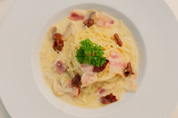 spaghetti carbonara on white dish, Creamy pasta carbonara with bacon bits and fresh parsley garnish served in white bowl. Classic Italian cuisine dish with rich sauce and herbs for dinner.