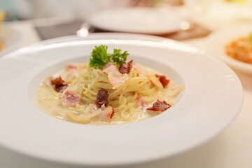 spaghetti carbonara on white dish, Creamy pasta carbonara with bacon bits and fresh parsley garnish served in white bowl. Classic Italian cuisine dish with rich sauce and herbs for dinner.