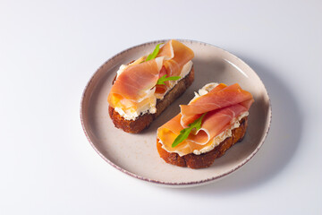 Two bruschettas with prosciutto, ricotta cheese and rucola on ciabatta bread. Olive and spices  decorated.