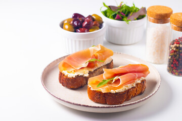 Two bruschettas with prosciutto, ricotta cheese and rucola on ciabatta bread. Olive and spices  decorated.