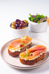 Two bruschettas with prosciutto, ricotta cheese and rucola on ciabatta bread. Olive and spices  decorated.