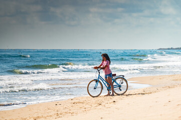 Fototapeta premium A woman is riding a bicycle on the beach. The sky is cloudy and the ocean is in the background