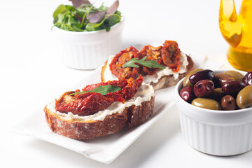 Two bruschettas with dried tomatoes, ricotta cheese and rucola on ciabatta bread. 