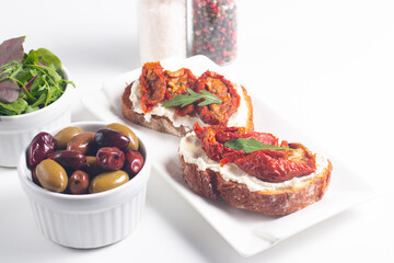 Two bruschettas with dried tomatoes, ricotta cheese and rucola on ciabatta bread. 