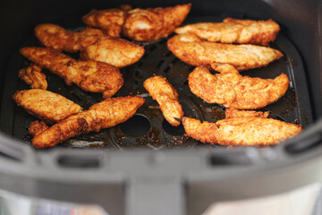 Crispy chicken strips. Fried in air fryer basket. Healthy oil free cooking. Homemade dinner preparation. Golden brown meat snack. Modern kitchen appliance in use.