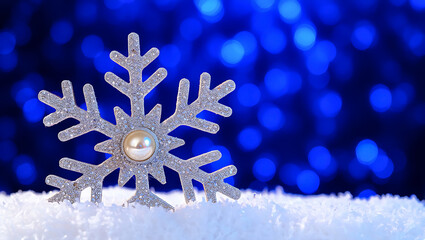 Sparkling silver snowflake with pearl center on snow and blurry blue bokeh background festive winter holiday season macro shot