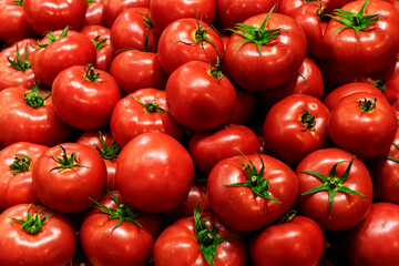Close up selective focus ob beautiful round ripe fresh red tomatoes displayed for sale at the local market, among other colourful vegetables
