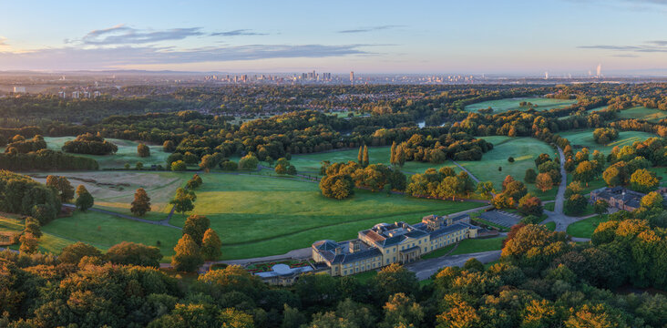Panoramic sunrise aerial of Heaton Park with woodland, green fields, and Manchester city skyline in view. - Powered by Adobe