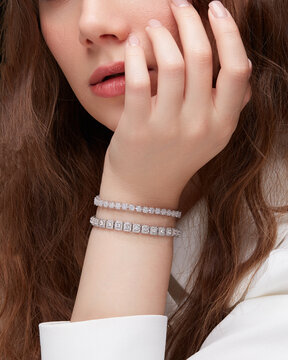 Close-up portrait of woman showing two diamond tennis bracelets on wrist touching face