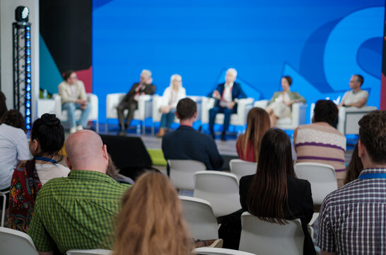 Audience watches panel discussion on stage with blue backdrop and seated experts sharing insights
