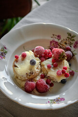 A plate of baked cheesecakes with sour cream and garnished with frozen berries on an antique porcelain plate, tablecloth, perfect for breakfast.