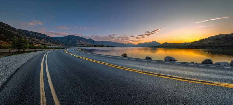 The winding road along a tranquil lake at sunset with mountainous backdrop. - Powered by Adobe