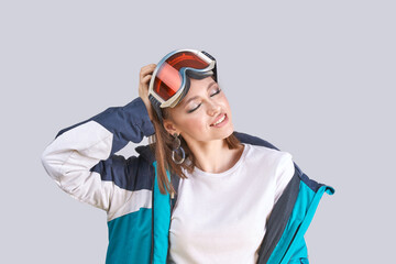 Young caucasian female wearing ski jacket and goggles in relaxed pose on gray background.