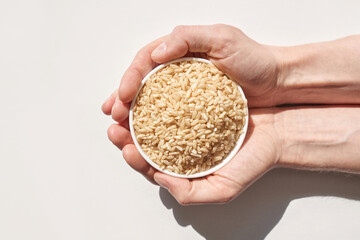 Caucasian hands holding bowl of brown rice against white background highlighting healthy organic...