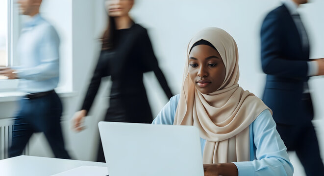 Focused businesswoman in hijab working on laptop in busy modern office diverse colleagues teamwork collaboration productivity success