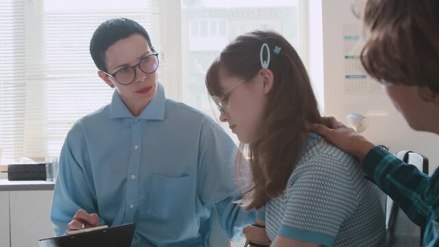 Teenage girl receiving support from her classmate and school councillor during group therapy session in classroom