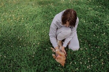 Fototapeta premium A young woman walks her playful puppy in a sunny garden, sharing a tender moment of love and care. Authentic, unaltered photography capturing the special bond between human and pet