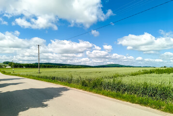 Świętokrzyskie krajobrazy wiosną. Błękitne niebo, Góry Świętokrzyskie, pola i droga biegnąca przez wieś. Spokojny, wiejski krajobraz z krętą drogą wzdłuż bujnych, zielonych pól pod niebieskim niebem.
