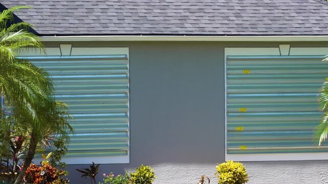 Steel panels mounted over house windows in Florida to shield against hurricane damage. Storm preparation and home protection
