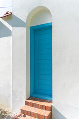 Blue wooden door with white wall and brick stairs in summer sunshine
