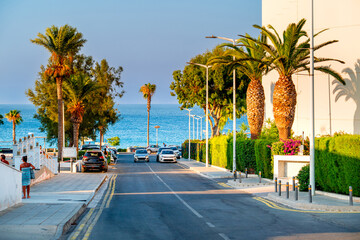 People in Cyprus seaside landscape with palm trees, hotels and turquoise Mediterranean Sea, Paralimni, Protaras.	
