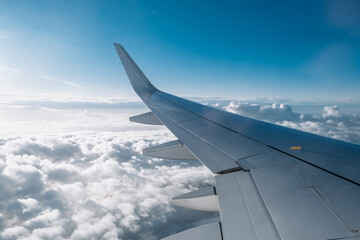 Fototapeta premium Airplane wing soaring above fluffy white clouds under a bright blue sky, capturing the essence of travel and adventure in the open atmosphere