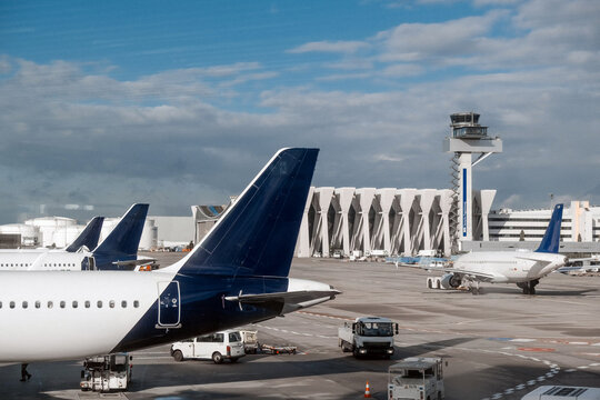 Airplanes parked at an airport terminal with control tower in the background, showcasing aviation infrastructure and busy air travel environment with clear blue sky