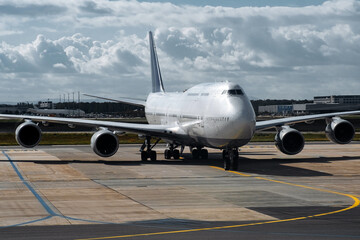 Fototapeta premium Large commercial airplane taxiing on runway under cloudy sky, showcasing aircraft design and engineering, symbolizing travel and aviation industry advancements