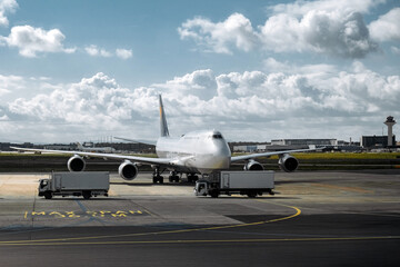 Obraz premium Large commercial airplane parked on airport tarmac, with service trucks nearby, showcasing aviation operations and airport logistics in a dynamic environment