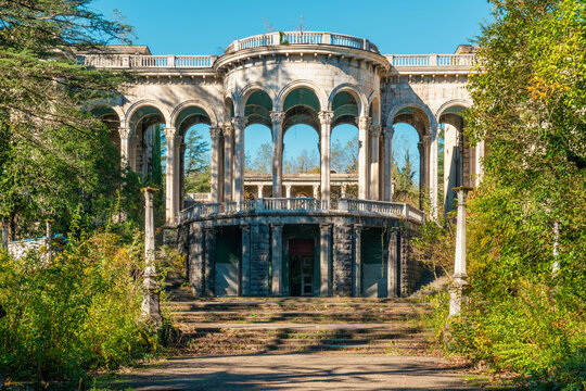 Abandoned neoclassical sanatorium in Tskaltubo, Georgia with grand staircase, arched columns and overgrown greenery on sunny day. Haunted house. Post apocalyptic, creepy and spooky