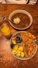Traditional Austrian cuisine served on a rustic wooden table: crispy Wiener schnitzel with parsley potatoes and lingonberry sauce, alongside hearty beef goulash with bread dumpling and fresh juice.