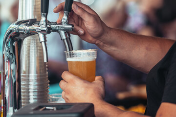 Close-up of a bartender pouring fresh draft beer into a plastic cup at an outdoor festival. Cold foamy lager being served from a tap, symbolizing refreshment, brewing and celebration