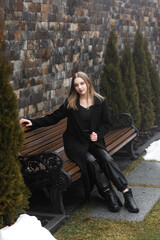A young girl in a black coat and leather pants in a park in winter