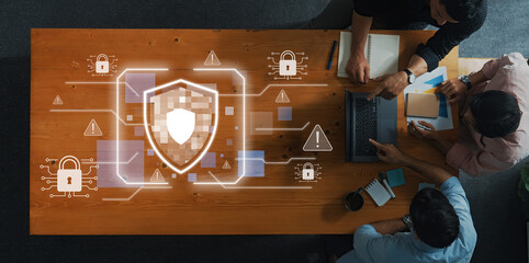 Professionals collaborate in a modern office, discussing cybersecurity strategies while digital symbols of data protection and safeguard measures surround them. Trope