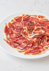Thin Slices of Jamon Iberico Arranged on White Round Plate for Serving