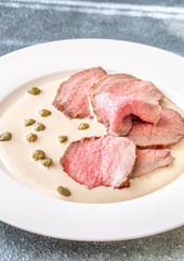 Elegant Vitello Tonnato with scattered capers and creamy sauce on plate