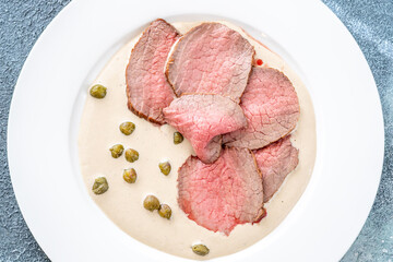 Elegant Vitello Tonnato with scattered capers and creamy sauce on plate