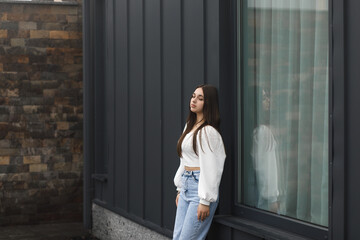 A girl in blue jeans near a metal wall with a window
