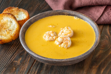 Rustic shrimp bisque with toasted baguette slices beside clay bowl