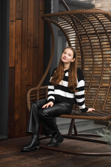 A girl in leather pants and a striped sweater near a wooden swing