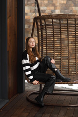 A girl in leather pants and a striped sweater near a wooden swing