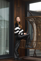 A girl in leather pants and a striped sweater near a wooden swing